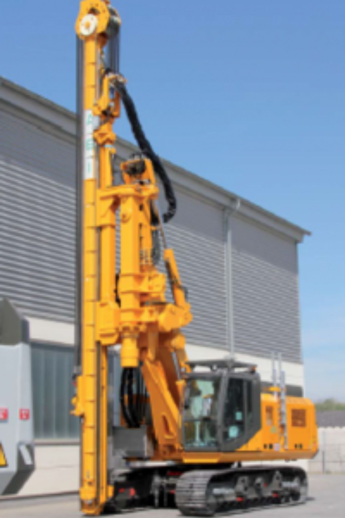 ABI telescopic leader mast machine in yellow finish near an industrial building